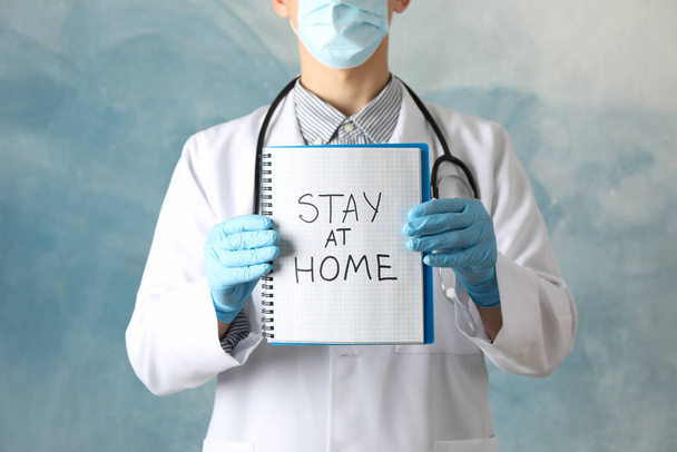 El médico sostiene el cuaderno con la inscripción Quédese en casa sobre fondo azul
 - Foto, imagen