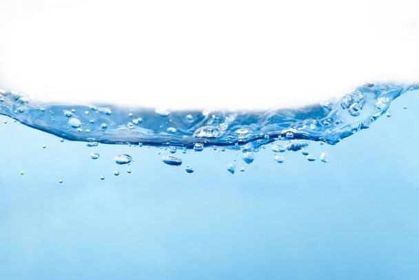 A vízhullám és a felület tiszta, kék színű, víz alatti kis buborékok és fehér háttér. - Fotó, kép