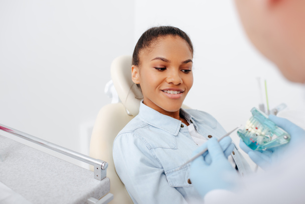 foco seletivo de mulher americana africana feliz em aparelho perto dentista segurando dentes modelo
  - Foto, Imagem