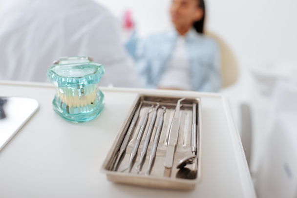 enfoque selectivo del modelo de dientes e instrumentos dentales cerca del dentista y el paciente afroamericano
  - Foto, Imagen