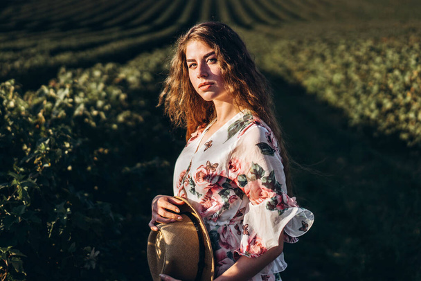 beautiful woman with long curly hair and freckles face on currant field background. Girl in a light dress walks in the summer sunny day. - Foto, Bild