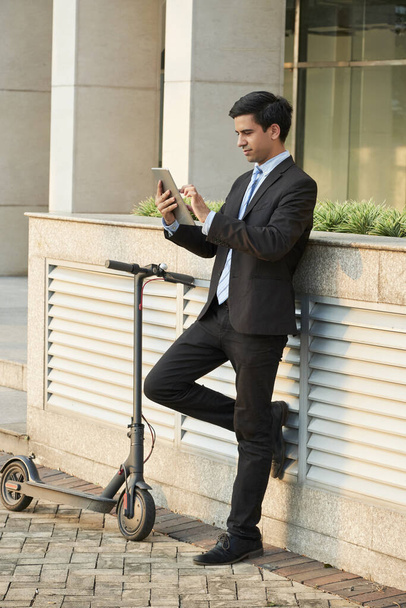Jovem empresário bonito confiante em pé ao ar livre e artigo de leitura no computador tablet
 - Foto, Imagem
