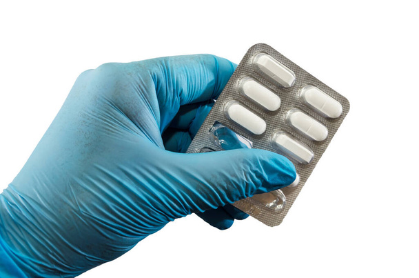 dłoń w niebieskiej rękawiczce trzyma blister z tabletkami odizolowanymi na białym tle. - Zdjęcie, obraz