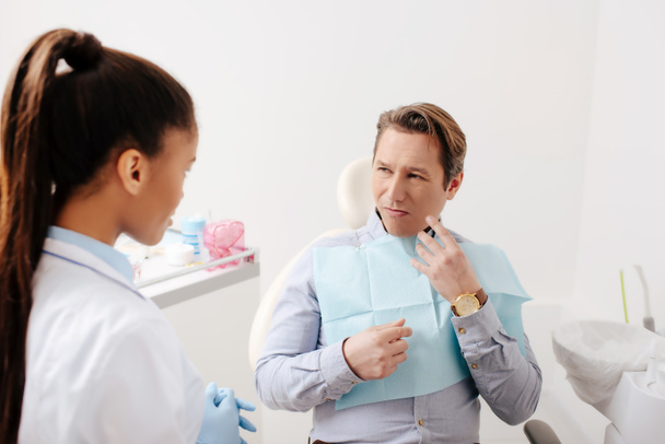 hombre con dolor de muelas mirando al dentista afroamericano en la clínica
  - Foto, Imagen