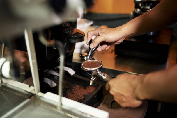 Barista hält Kaffeestampfer und Stampfen Arabica-Boden in Espresso Doppelauslauf Portafilter vor dem Brauen mit Espressomaschine - Foto, Bild