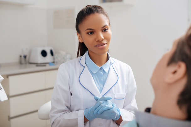 selective focus of attractive african american dentist with clenched hands looking at patient  - Foto, Imagem