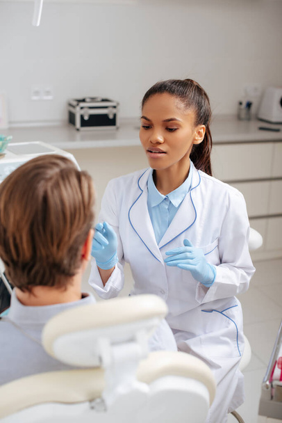 selektiver Fokus attraktiver afrikanisch-amerikanischer Zahnarzt gestikuliert in der Nähe des Patienten  - Foto, Bild