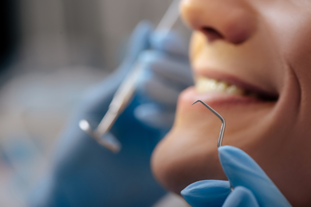 обрезанный вид стоматолога в латексных перчатках, держащих стоматологические инструменты рядом с веселым человеком
  - Фото, изображение