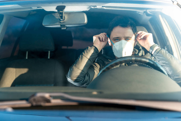 El hombre pone máscara médica en la cara en el coche. prevención contra el coronavirus covid-19. cuarentena en el momento de la epidemia viral
 - Foto, Imagen