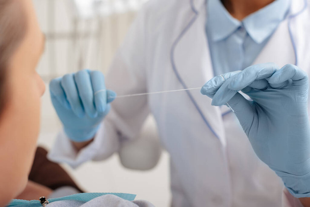 селективний фокус стоматолога в латексних рукавичках, що тримає зубну нитку біля пацієнта
  - Фото, зображення
