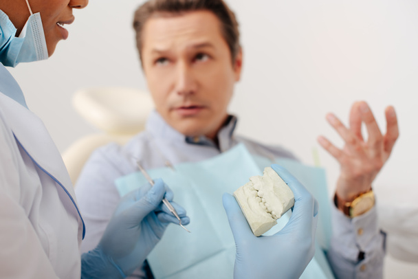 messa a fuoco selettiva del dentista afroamericano in guanti di lattice con modello di denti e strumento dentale vicino all'uomo
   - Foto, immagini
