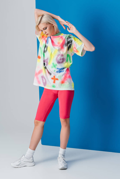 tyylikäs nainen poseeraa neon vaaleanpunainen pyörä shortsit ja värikäs t-paita harmaa ja sininen
  - Valokuva, kuva