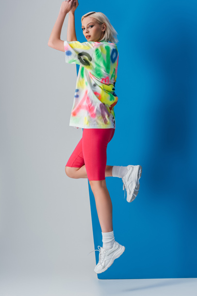 attractive girl jumping in neon pink bike shorts and colorful t-shirt on grey and blue  - Foto, Imagem