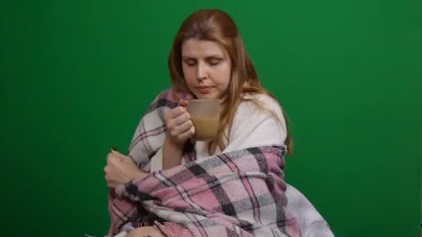 Sick woman wrapped in warm blanket drinking hot tea. Cough. Chill. COVID Danger of coronavirus pandemic 2019-ncov. Shot on a green isolated background. Quarantine, fears. Chromakey. - Záběry, video