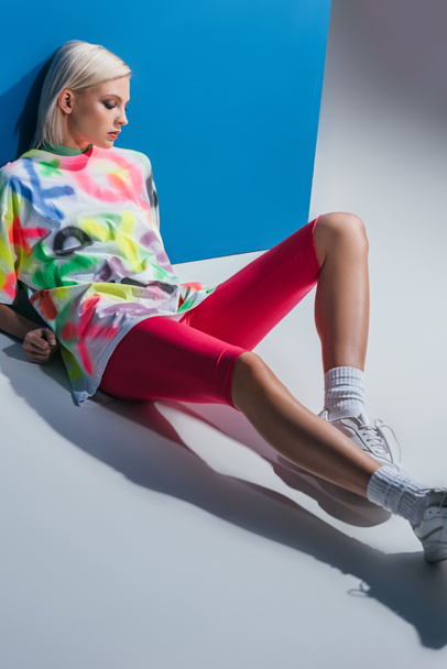 beautiful fashionable girl posing in neon pink bike shorts and colorful t-shirt on grey and blue  - Fotoğraf, Görsel
