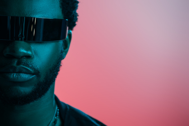 stylish african american man in futuristic sunglasses posing on pink in blue light  - Photo, Image