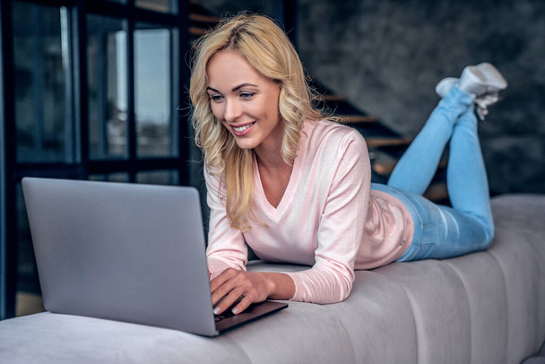 Attractive young woman spending time at home. Relaxing while lying on sofa with laptop - Photo, Image