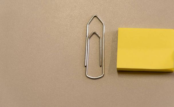 Un escritorio de oficina y un gran clip de papel y una almohadilla amarilla en él. Material de oficina y papelería
 - Foto, Imagen