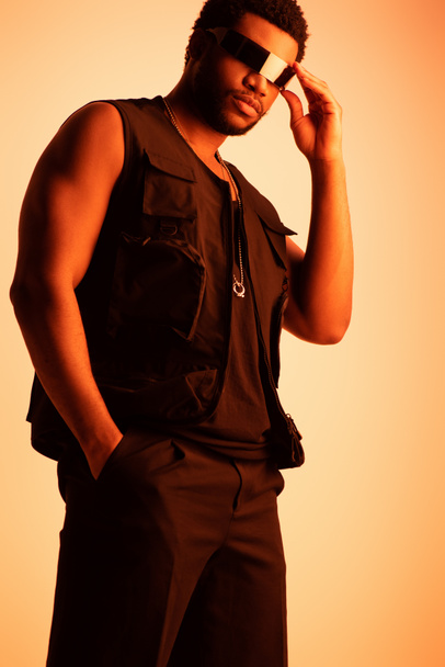 modelo masculino afroamericano guapo posando en gafas de sol futuristas en naranja
 - Foto, imagen