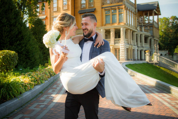 The groom holds the bride in his arms at the wedding, happy newlyweds - Фото, зображення