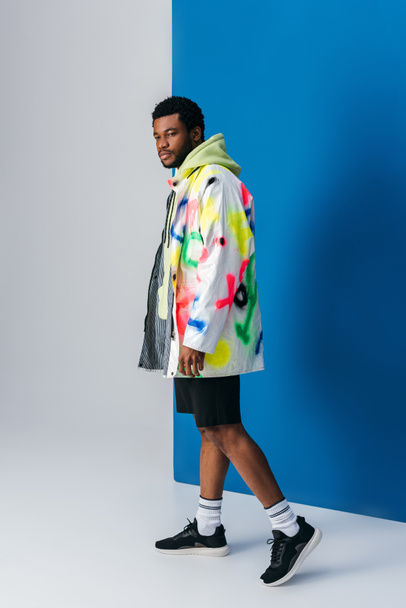 african american man posing in colorful futuristic clothes on grey and blue - Fotó, kép