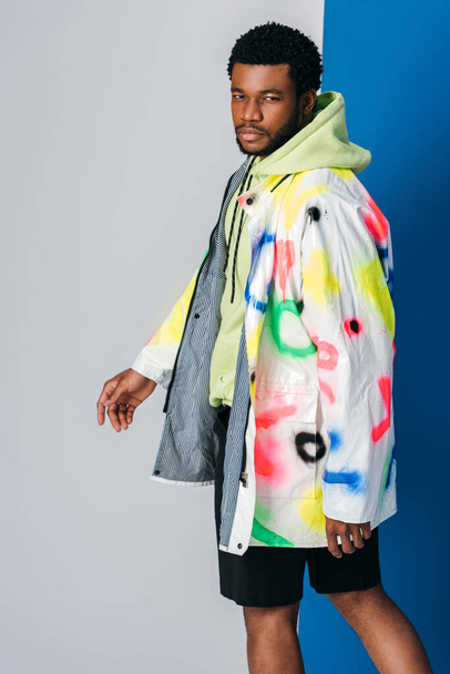 fashionable young african american man posing in colorful futuristic clothes on grey and blue - Photo, Image