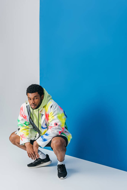 stylish young african american man posing in colorful futuristic clothes on grey and blue - Valokuva, kuva