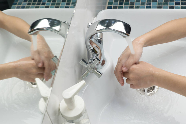 子供は水道水で浴槽に手を洗い、鏡の中の手の反射、感染症、ウイルス、コロナウイルスのパンデミックからの保護措置 - 写真・画像