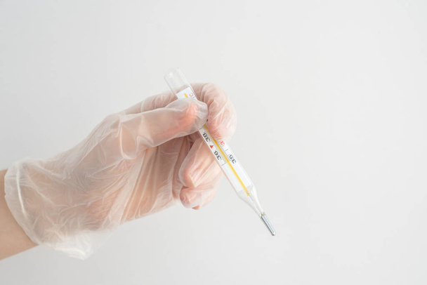 рука в білій медичній рукавичці тримає медичний термометр ртуті, заходи проти вірусів, коронавірусу, епідемії, концепції охорони здоров'я
 - Фото, зображення