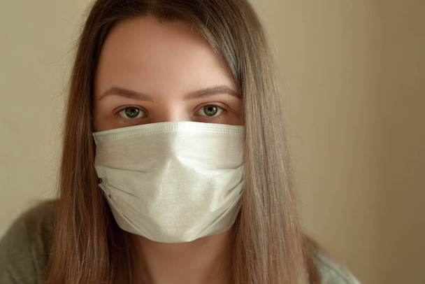 Young woman with protection medical mask looking at camera. Stay at home for quarantine to prevent coronavirus spread. Concept for protect from infection, respiratory disease, virus or bacteria. - 写真・画像