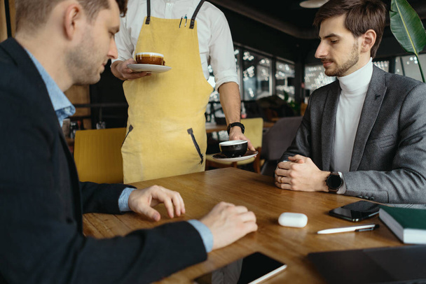 Ober serveert koffie aan mannelijke klanten in het restaurant - Foto, afbeelding