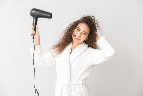 Beautiful young African-American woman with blow dryer on light background - Fotografie, Obrázek