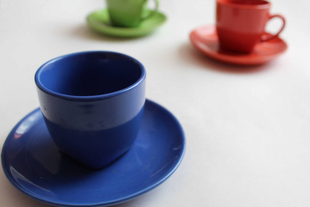 una Copa azul o verde una jarra con una sartén se levanta sobre la mesa en un fondo blanco detrás de usted puede ver otras dos jarras rojas y azul o verde mañana Desayuno té o café. - Foto, imagen