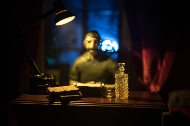 Realistyczny salon z meblami i oknem w nocy. Mężczyzna siedzący na stole w ciemnym pokoju. Skupienie selektywne. - Zdjęcie, obraz