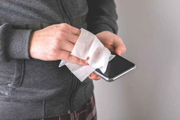 Les mains de l'homme essuyant téléphone portable avec lingette humide avec désinfectant. Hygiène protection contre le virus corona. Concept de prévention du coronavirus
. - Photo, image