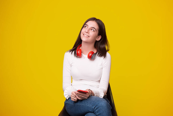 happy young woman looking away and holding smartphone over yellow background - Foto, Imagen
