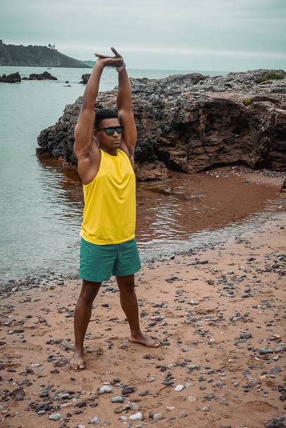 The young fit man with sunglasses working out with the ocean and the rocks in a background - Foto, Imagem