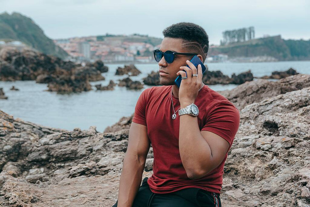 A beautiful shot of a young man with sunglasses talking on the phone on the beach - Valokuva, kuva
