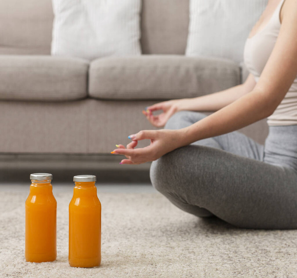 Unrecognizable young woman doing yoga at home and drinking fresh juice - Фото, зображення