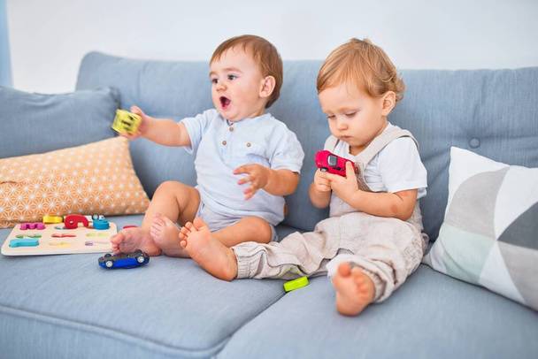 Beautiful toddlers sitting on the sofa playing with toys at home - Fotó, kép