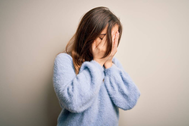 泣きながら手で顔を覆う悲しい表情で孤立した背景の上に立つカジュアルな冬のセーターを着た美しい若い女性。うつ病の概念. - 写真・画像