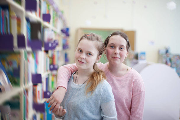 Adolescente niñas cerca de estantes con libros en la biblioteca
. - Foto, imagen