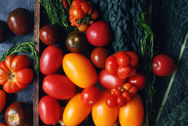 Meng van kleurrijke rauwe verse tomaten en kruiden op donkere stenen tafel en oude houten plank, gezonde levensstijl, biologisch voedingsconcept, bovenaanzicht - Foto, afbeelding