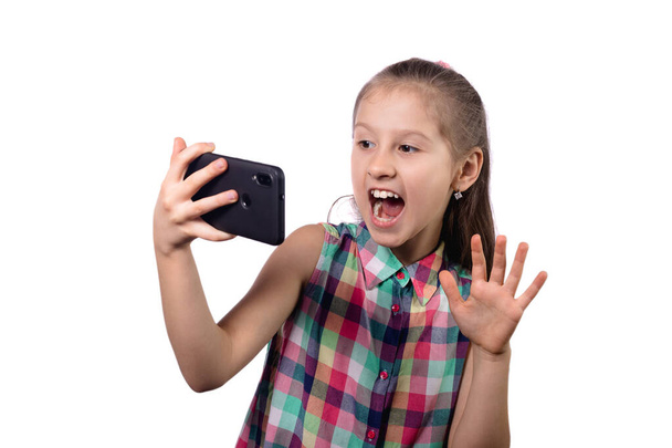 かわいい女の子が彼女の携帯電話で自撮りしている。白い背景のスタジオ写真 - 写真・画像