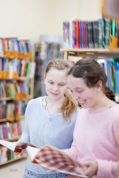 Meninas adolescentes perto de prateleiras com livros na biblioteca
. - Foto, Imagem