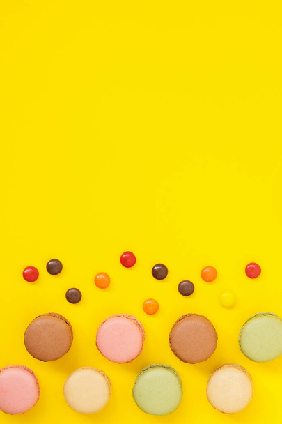 Galletas francesas macaron de diferentes colores sobre fondo amarillo. Caramelos rojos. Copiar espacio
. - Foto, imagen