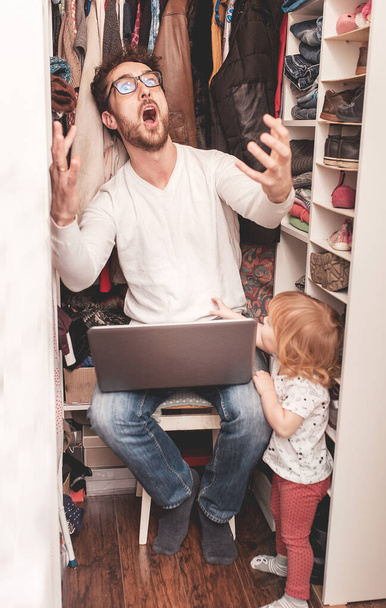 Kiireinen isä yrittää löytää rauhallinen paikka vaatekaappi piiloutua lapsilta työtä kannettavan tietokoneen. Pysy kotona. Karanteeni. Freelancer
. - Valokuva, kuva