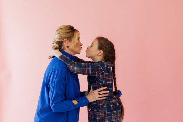 Mamá y su hija se ríen y se besan sobre un fondo rosa
 - Foto, Imagen