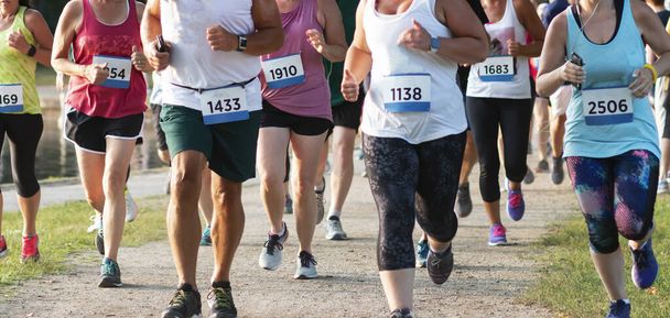 Un gran grupo de corredores corriendo hacia la cámara mientras corrían en una carrera de senderos de verano alrededor de un Parque Estatal Belmont Lake
. - Foto, Imagen