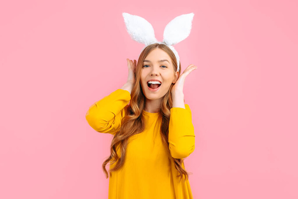 happy Easter. Happy stylish woman in Easter Bunny ears, covers her ears with her hands, on an isolated pink background - Фото, зображення